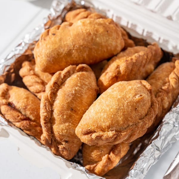 A close-up of golden-brown, crispy Filipino empanadas in a foil-lined takeout container.
