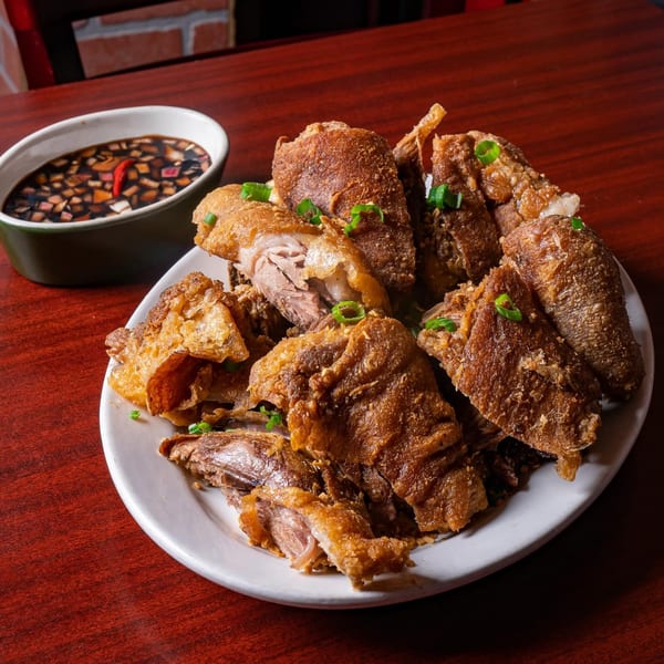 Crispy Filipino deep-fried pork hock (Crispy Pata) with a side of dipping sauce on a wooden table.