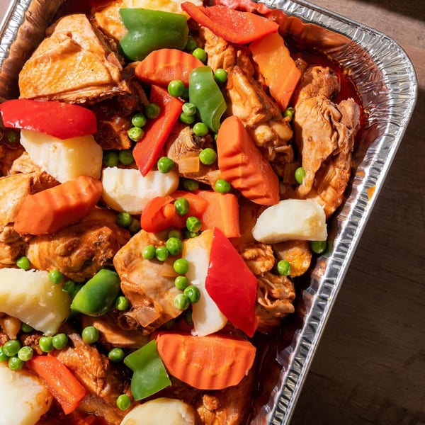 Filipino chicken adobo with potatoes, carrots, peas, and bell peppers in a foil tray.