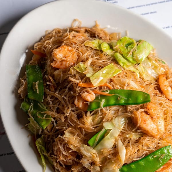 Filipino pancit bihon with thin noodles, shrimp, cabbage, and snow peas on a white plate.