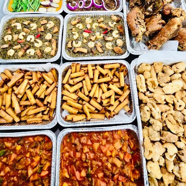 A variety of Filipino dishes in foil trays, including fried pork, lumpia, and stews.