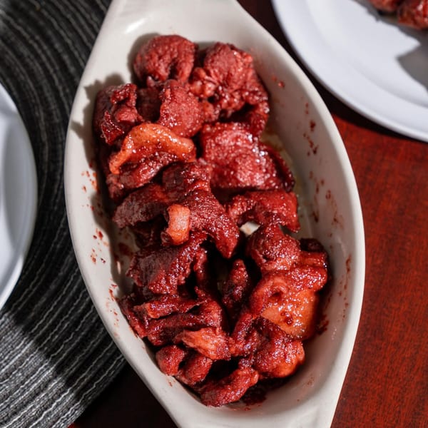 A white oval dish filled with bright red Filipino tocino pork slices, glistening under direct light.