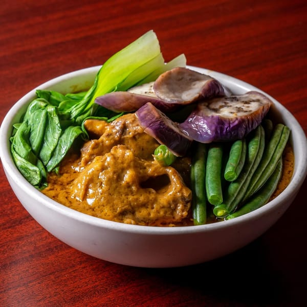 A bowl of Filipino Kare-Kare with peanut sauce, meat, green beans, bok choy, and eggplant.