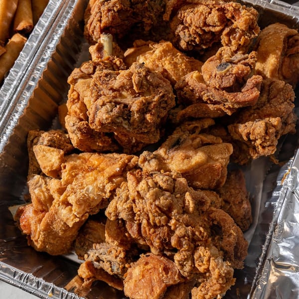Crispy fried chicken pieces and lumpia in a foil takeout container from Matthew's Grill.